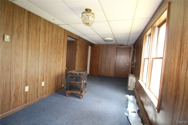 unfurnished room featuring an AC wall unit, a paneled ceiling, wooden walls, and dark colored carpet