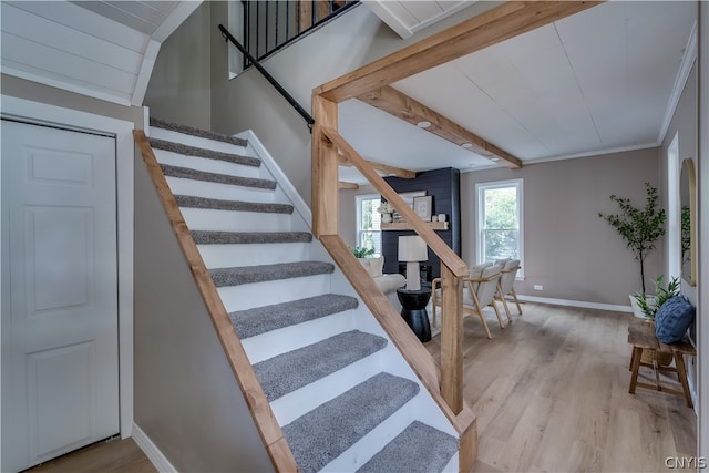 stairway with light hardwood / wood-style floors, crown molding, and beamed ceiling