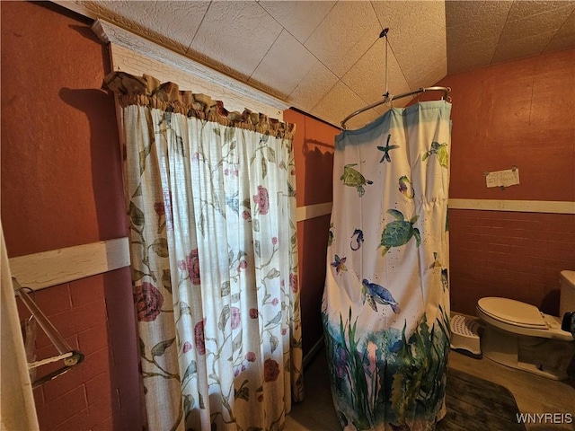 full bath featuring wainscoting, toilet, tile walls, and a shower with shower curtain