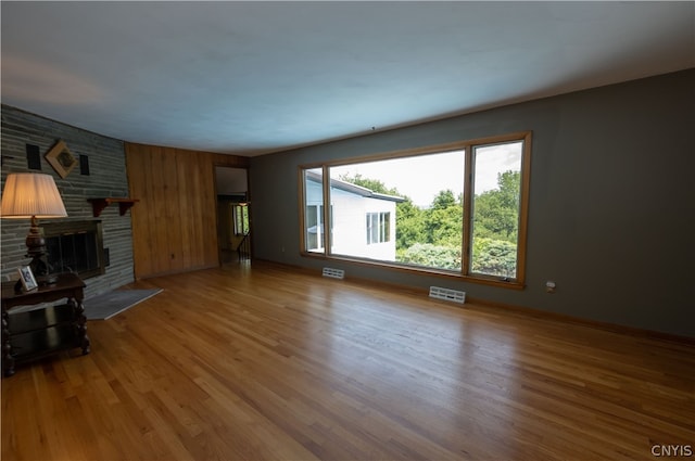 unfurnished living room featuring a brick fireplace, hardwood / wood-style flooring, and wooden walls