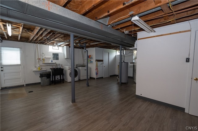 basement featuring water heater, washer and clothes dryer, electric panel, and hardwood / wood-style flooring