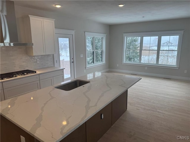 kitchen with white cabinets, light stone counters, and wall chimney range hood