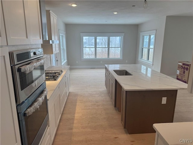 kitchen with stainless steel appliances, a kitchen island, light stone counters, white cabinets, and light wood-type flooring