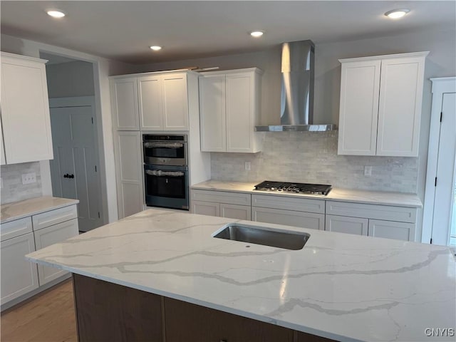 kitchen with appliances with stainless steel finishes, tasteful backsplash, light stone counters, wall chimney range hood, and white cabinetry