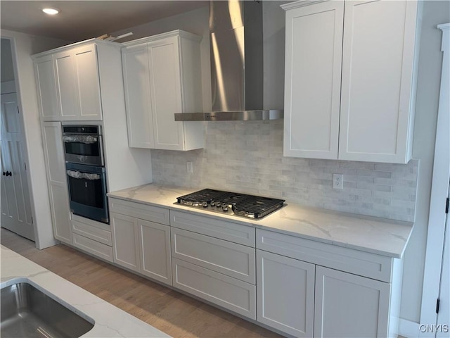 kitchen featuring wall chimney exhaust hood, white cabinetry, and appliances with stainless steel finishes