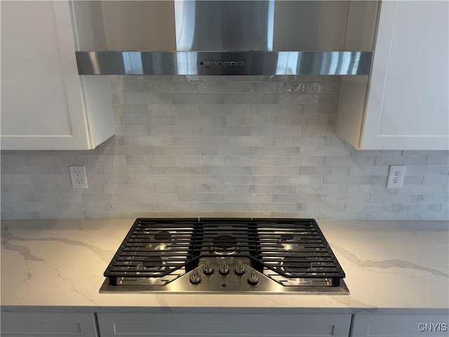 details featuring light stone countertops, wall chimney range hood, stainless steel gas cooktop, and tasteful backsplash