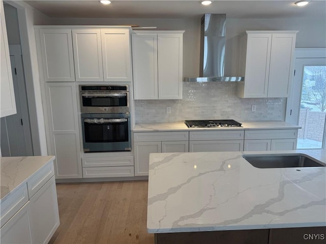 kitchen with backsplash, stainless steel appliances, white cabinetry, and wall chimney range hood