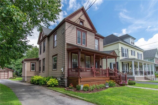 victorian-style house with covered porch, an outbuilding, a garage, and a front yard