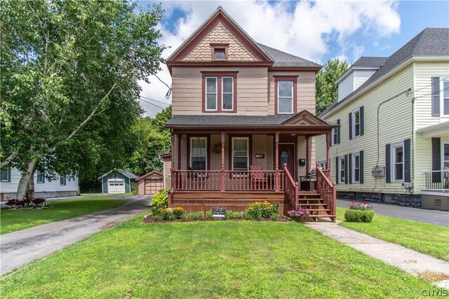 victorian-style house featuring a garage, an outbuilding, a front lawn, and covered porch