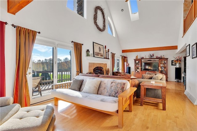 living room with a high ceiling, light wood-type flooring, and a skylight