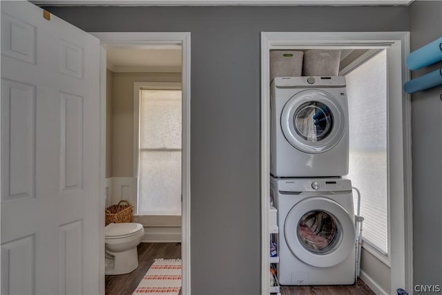 laundry area with a healthy amount of sunlight, stacked washing maching and dryer, and dark hardwood / wood-style flooring