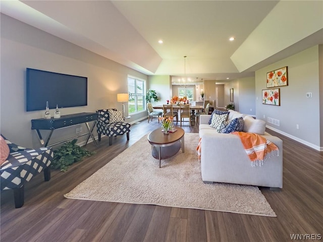 living room featuring a raised ceiling, vaulted ceiling, dark wood-type flooring, and a chandelier