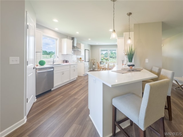 kitchen featuring sink, white cabinetry, stainless steel dishwasher, pendant lighting, and wall chimney range hood