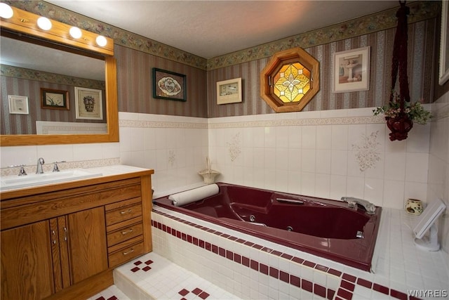 full bath with tile walls, a jetted tub, vanity, and wallpapered walls