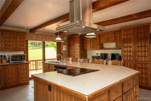 kitchen featuring stainless steel microwave, brown cabinetry, a sink, island range hood, and beamed ceiling