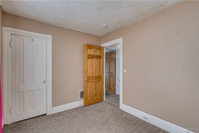 unfurnished bedroom with light carpet, a closet, and a textured ceiling