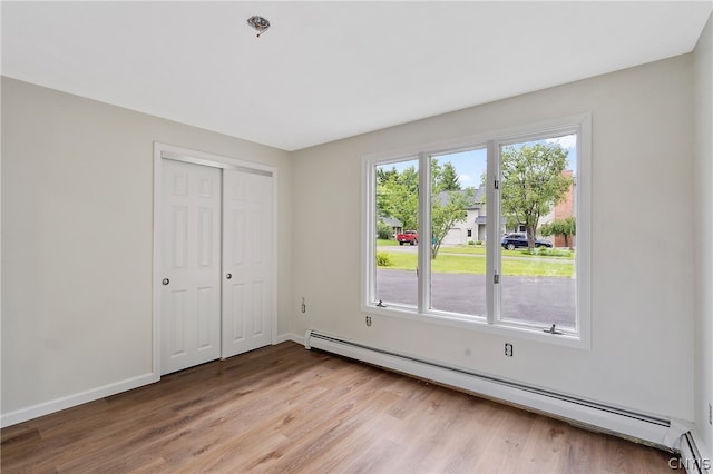 unfurnished bedroom featuring light wood-type flooring, a closet, and baseboard heating