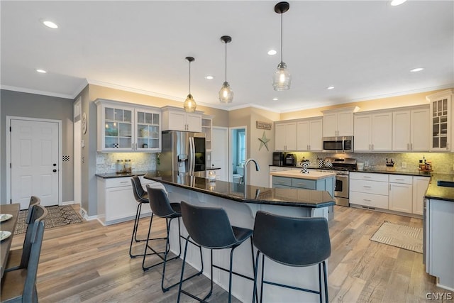 kitchen with pendant lighting, appliances with stainless steel finishes, a kitchen island with sink, a kitchen bar, and light wood-type flooring