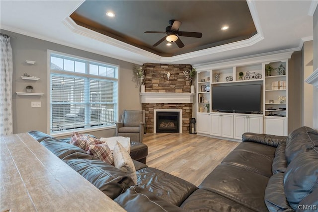 living room featuring crown molding, a stone fireplace, a raised ceiling, and hardwood / wood-style flooring