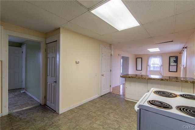 kitchen featuring a drop ceiling, light tile patterned flooring, white cabinets, light stone counters, and stove