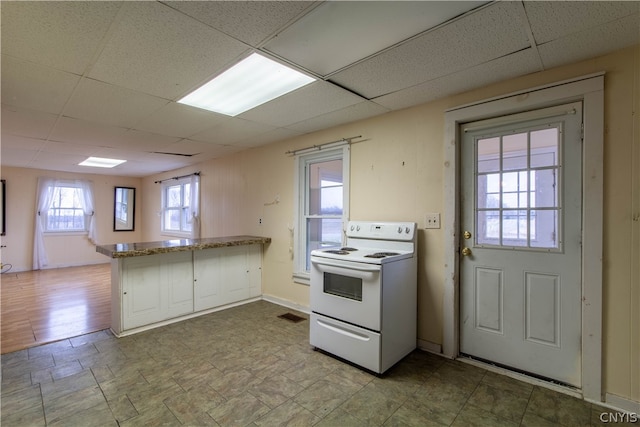 kitchen with kitchen peninsula, white range with electric stovetop, light stone counters, tile patterned floors, and a paneled ceiling