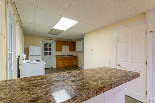 kitchen featuring sink, dark tile patterned floors, white appliances, and a drop ceiling