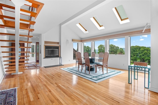 unfurnished dining area with light wood-type flooring, a healthy amount of sunlight, a skylight, and high vaulted ceiling