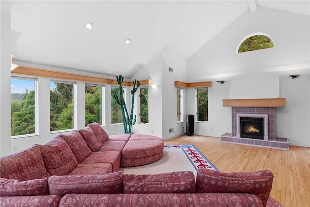 living room featuring high vaulted ceiling, light wood-type flooring, beamed ceiling, and a tile fireplace