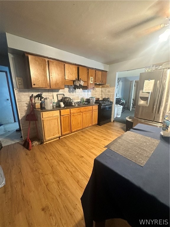 kitchen featuring backsplash, stainless steel fridge, black range oven, and light wood-type flooring