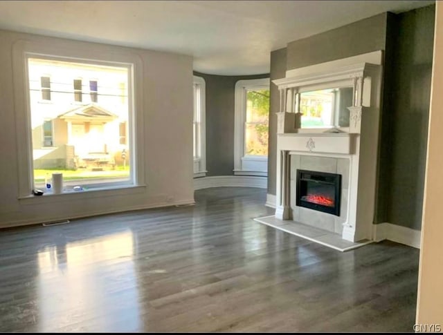 unfurnished living room featuring a tiled fireplace, a healthy amount of sunlight, and dark hardwood / wood-style floors