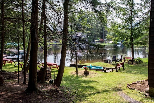 surrounding community with a boat dock, a water view, and a lawn