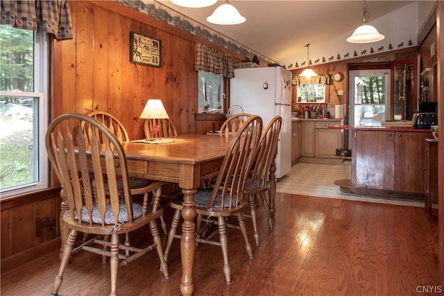 dining room with lofted ceiling, wood-type flooring, wood walls, and plenty of natural light