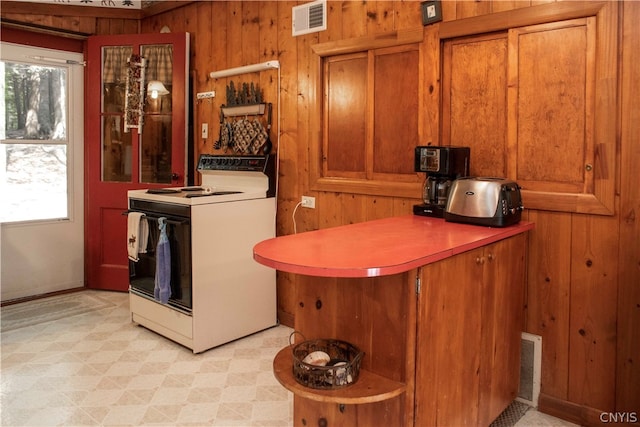 interior space with wood walls, white electric range oven, and light tile patterned floors