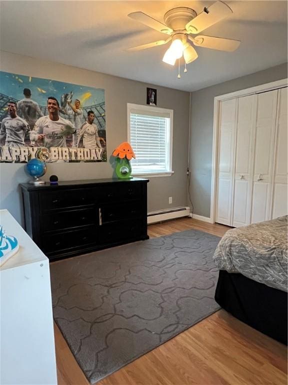 bedroom featuring a baseboard heating unit, baseboards, wood finished floors, a closet, and a ceiling fan