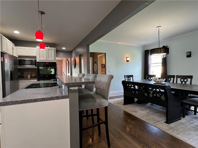 kitchen with a breakfast bar, dark wood-style flooring, ornamental molding, black appliances, and white cabinets