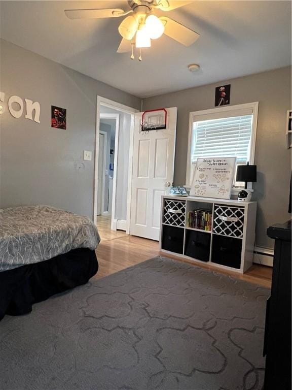 bedroom with light wood-style floors, baseboard heating, and a ceiling fan