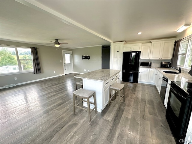 kitchen with a kitchen bar, sink, black appliances, a center island, and dark hardwood / wood-style floors