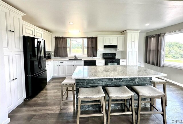 kitchen featuring a breakfast bar, sink, black appliances, a center island, and dark hardwood / wood-style floors