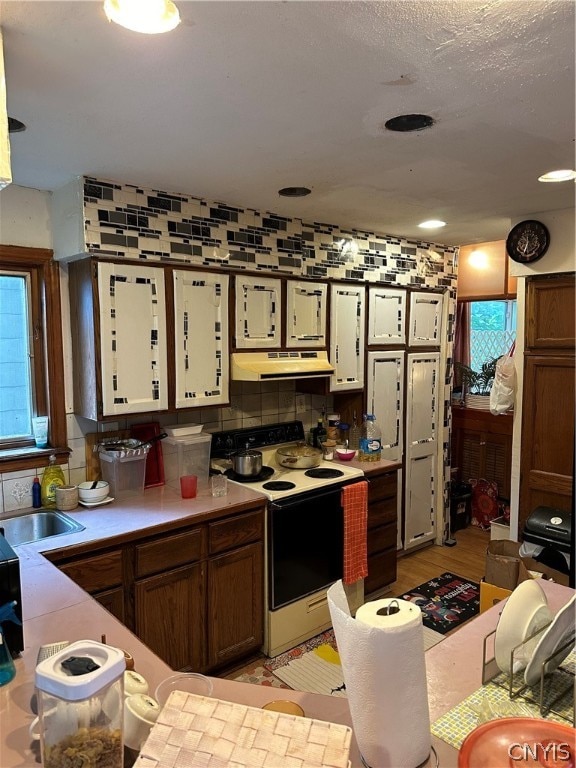 kitchen featuring sink, extractor fan, white electric stove, light hardwood / wood-style floors, and tasteful backsplash