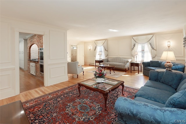 living room featuring baseboard heating, light wood-type flooring, and ornamental molding