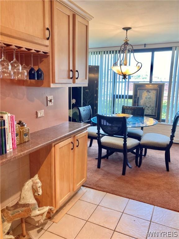 kitchen featuring light tile patterned floors, light colored carpet, light brown cabinets, and decorative light fixtures