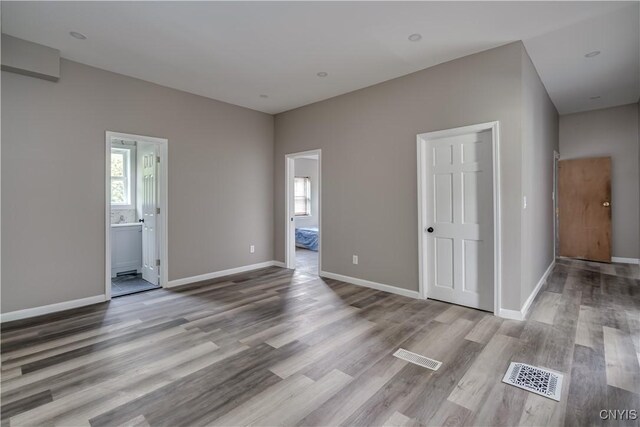 unfurnished bedroom with ensuite bath and hardwood / wood-style floors