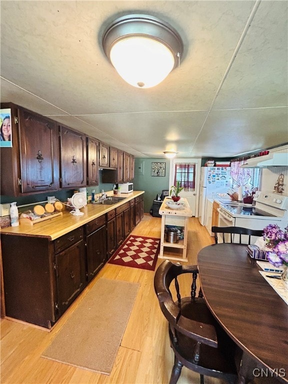 kitchen with dark brown cabinets, white appliances, sink, range hood, and light hardwood / wood-style floors