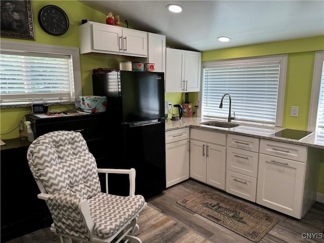 kitchen featuring dark wood-type flooring, white cabinets, light stone countertops, sink, and black refrigerator