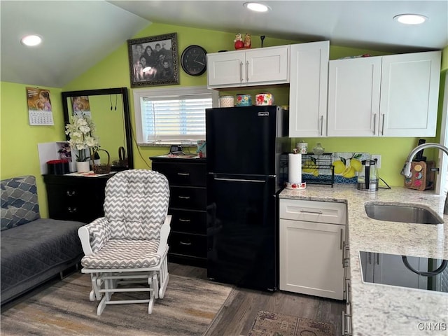 kitchen featuring hardwood / wood-style floors, white cabinetry, sink, black fridge, and vaulted ceiling