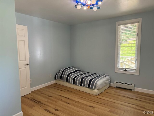 bedroom with an inviting chandelier, light hardwood / wood-style floors, and a baseboard radiator