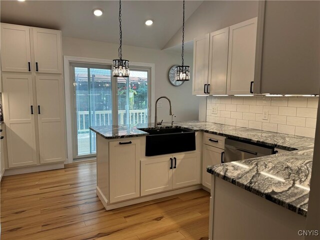 kitchen featuring vaulted ceiling, stone countertops, light hardwood / wood-style floors, decorative light fixtures, and kitchen peninsula