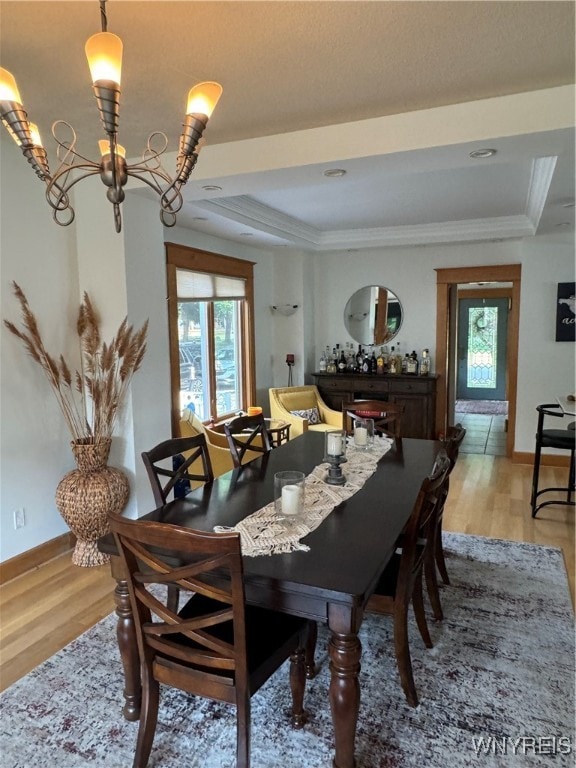 dining room with light hardwood / wood-style flooring, a healthy amount of sunlight, a raised ceiling, and a chandelier