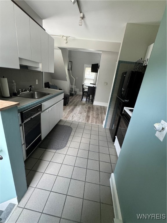 kitchen featuring white cabinets, rail lighting, sink, light hardwood / wood-style flooring, and backsplash