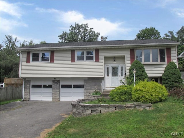 raised ranch with driveway, stone siding, a garage, and a front yard